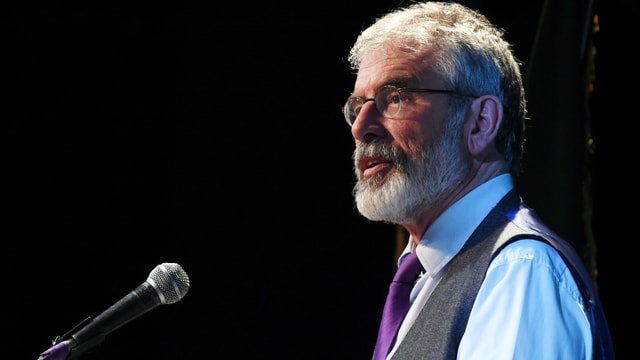 Adams spricht vor schwarzem Hintergrund in ein Mikrofon, Profil-Aufnahme. Adams spricht vor schwarzem Hintergrund in ein Mikrofon, Profil-Aufnahme.