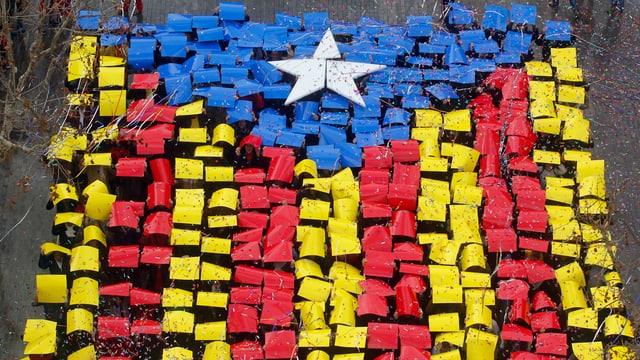 Mit roten, gelben, blauben und weissen Plakaten formen Katalanen ihre Regionalflagge auf einer Strasse (Aufnahme von oben). Mit roten, gelben, blauben und weissen Plakaten formen Katalanen ihre Regionalflagge auf einer Strasse (Aufnahme von oben).