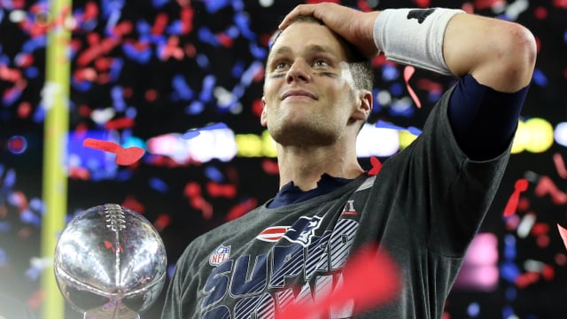 Tom Brady mit dem Super-Bowl-Pokal im Konfettiregen. Er fasst sich mit der linken Hand an den Kopf.