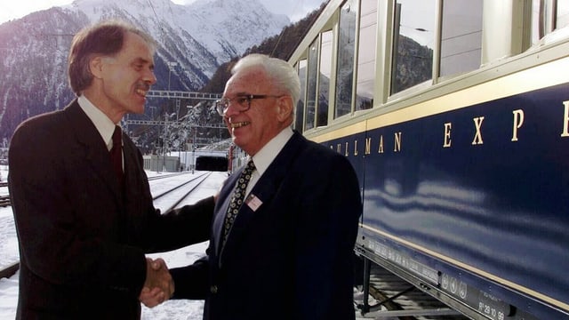 Moritz Leuenberger (san.) e dr. Leon Schlumpf tar la festa uffiziala d'avertura. Moritz Leuenberger (san.) e dr. Leon Schlumpf tar la festa uffiziala d'avertura.
