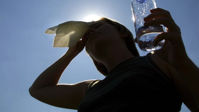 Person mit einem Trinkgefäss in der Hand wischt sich den Schweiss von der Stirn. Person mit einem Trinkgefäss in der Hand wischt sich den Schweiss von der Stirn.