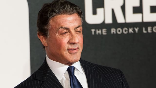 Sylvester Stallone in Anzug vor Foto-Wand. Sylvester Stallone in Anzug vor Foto-Wand.
