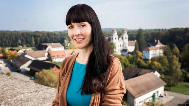 Frau mit langen schwarzen Haaren steht lächelnd vor einer Mauer. Frau mit langen schwarzen Haaren steht lächelnd vor einer Mauer.
