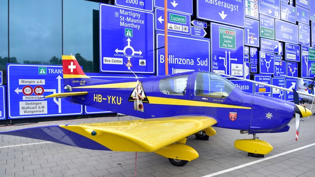 Die Fassade des Verkehrshauses Luzern, mit Schildern behangen, ein Flugzeug davor Die Fassade des Verkehrshauses Luzern, mit Schildern behangen, ein Flugzeug davor