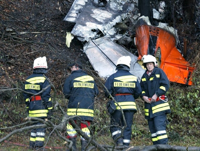 Vier Feuerwehrmänner vor dem Wrack mit einer orange-farbenen Heckflosse.