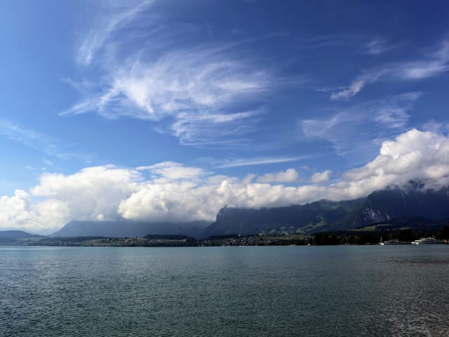 See dahinter Bergkette in Wolken, darüber blauer Himmel.