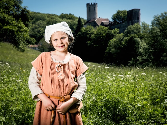 Junges Mädchen in mittelalterlicher Kleidung auf einer Wiese mit einer Burg im Hintergrund Junges Mädchen in mittelalterlicher Kleidung auf einer Wiese mit einer Burg im Hintergrund