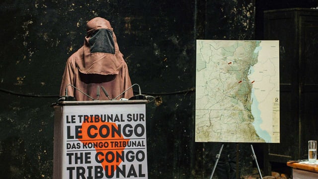 EIn evermumte PErson an einem Podium mit der Aufschrift "Le Tribunal sur le Conge" EIn evermumte PErson an einem Podium mit der Aufschrift "Le Tribunal sur le Conge"
