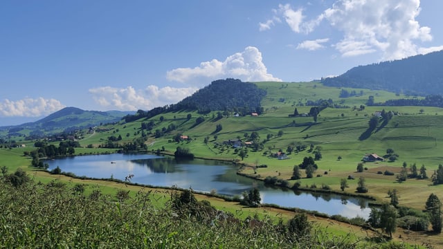 Der blaue Hüttnersee mitten in grünen Wiesen, darüber der blaue Himmel mit ersten Quellwolken. Der blaue Hüttnersee mitten in grünen Wiesen, darüber der blaue Himmel mit ersten Quellwolken.