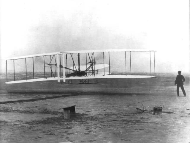 Schwarz-Weiss-Aufnahme mit den Gebrüdern Wright und einem Flugzeug