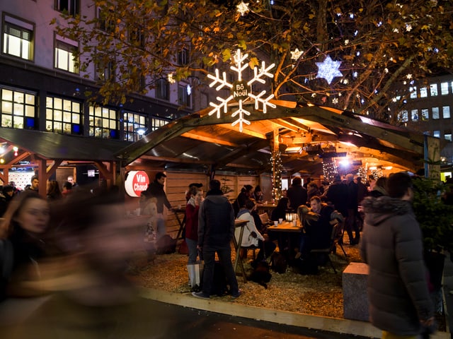 Menschen sitzen vor einem Häuschen auf dem Lausanner Weihnachtsmarkt Menschen sitzen vor einem Häuschen auf dem Lausanner Weihnachtsmarkt