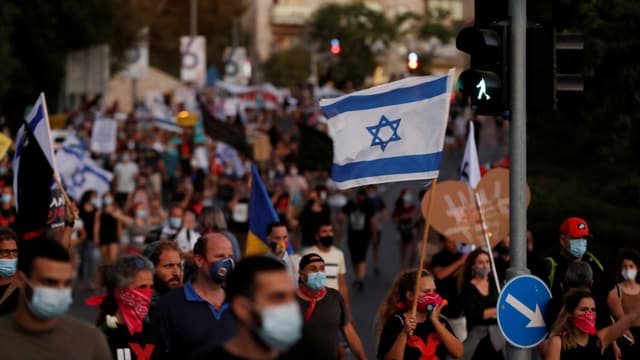 Protestierende tragen Schutzmasken und halten Israels Landesflagge. Protestierende tragen Schutzmasken und halten Israels Landesflagge.