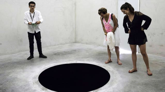 Im Museum: Drei Leute schauen auf ein schwarzes Loch im Boden. Im Museum: Drei Leute schauen auf ein schwarzes Loch im Boden.