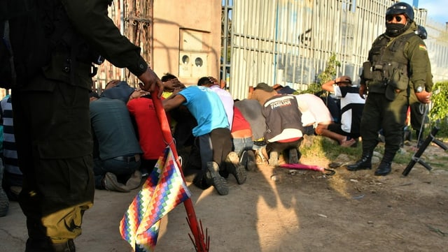 Kniende Menschen mit Händen über Kopf. Daneben Polizei. Kniende Menschen mit Händen über Kopf. Daneben Polizei.