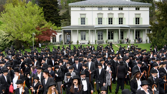Hunderte als Charly Chaplin verkleidete Menschen versammeln sich in einem Garten Hunderte als Charly Chaplin verkleidete Menschen versammeln sich in einem Garten
