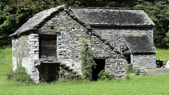 Ein Steinhaus steht in einer Wiese.