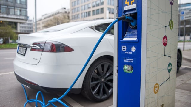 Ein weisses Auto wird an der Zapfsäule mit Strom betankt. Ein weisses Auto wird an der Zapfsäule mit Strom betankt.