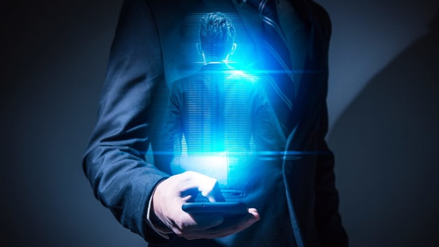 Ein Mann hält ein Smartphone in der Hand, vor ihm erscheint eine Projektion seiner selbst. Ein Mann hält ein Smartphone in der Hand, vor ihm erscheint eine Projektion seiner selbst.