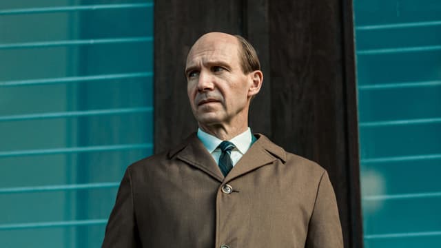 Ein Mann mit Halbglatze trägt ein Krawatte und einen Mantel und blickt ernst auf die Seite. Ein Mann mit Halbglatze trägt ein Krawatte und einen Mantel und blickt ernst auf die Seite.