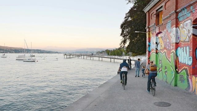 Velofahrer, direkt am See. Im Hintergrund: ein langer Steg Velofahrer, direkt am See. Im Hintergrund: ein langer Steg