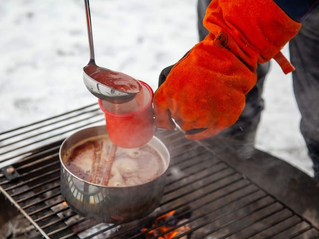 Mit einem Lederhandschuh wird aus einer Pfanne, die auf dem Feuer steht Orangenpunsch serviert. Mit einem Lederhandschuh wird aus einer Pfanne, die auf dem Feuer steht Orangenpunsch serviert.