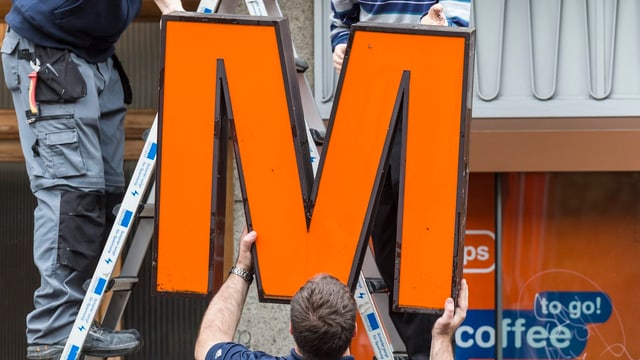 Arbeiter montieren ein Migros-Logo ab. Arbeiter montieren ein Migros-Logo ab.