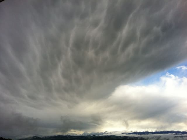 Bewölkter Himmel, an der Unterseite sackartige Strukturen. Wolkenwand zieht weiter, dahinter blauer Himmel.