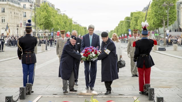 John Kerry mit einem Blumenkranz und einigen unbekannten Personen