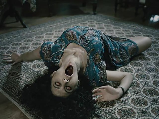 FIlmstill aus einem Horrorfilm: Eine Frau wälzt sich am Boden. FIlmstill aus einem Horrorfilm: Eine Frau wälzt sich am Boden.