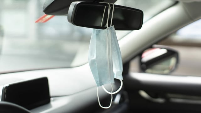 Zwei Schutzmasken hängen am Innenspiegel eines Autos. Zwei Schutzmasken hängen am Innenspiegel eines Autos.