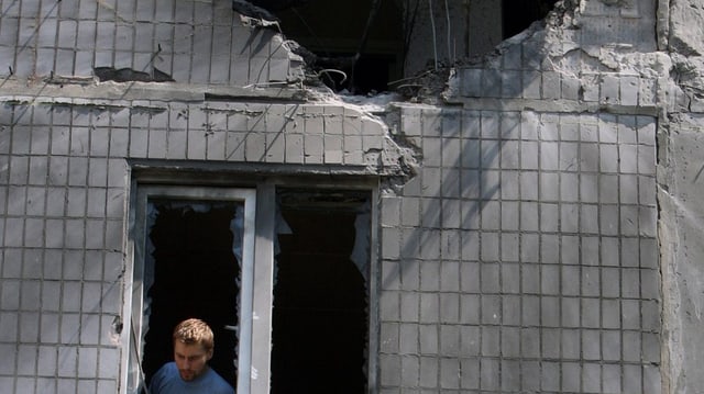 Mann schaut aus dem Fenster eines beschädigten Wohnhauses in Donezk Mann schaut aus dem Fenster eines beschädigten Wohnhauses in Donezk
