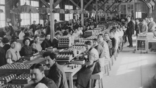 Fabrikhalle, Männer und Frauen, Munitionskisten, hochstehende Granaten Fabrikhalle, Männer und Frauen, Munitionskisten, hochstehende Granaten