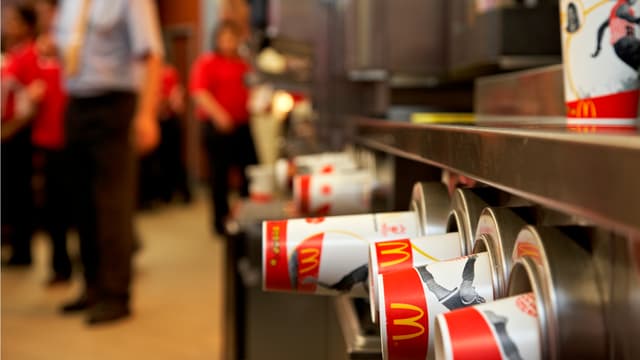 Mc Donalds Pappbecher und im Hintergrund unscharf Mitarbeiter. Mc Donalds Pappbecher und im Hintergrund unscharf Mitarbeiter.
