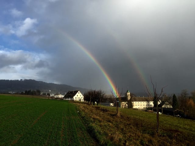 Blauer Himmel, dunkle Regenwolken und zwei Regenbogen über dem Kloster.