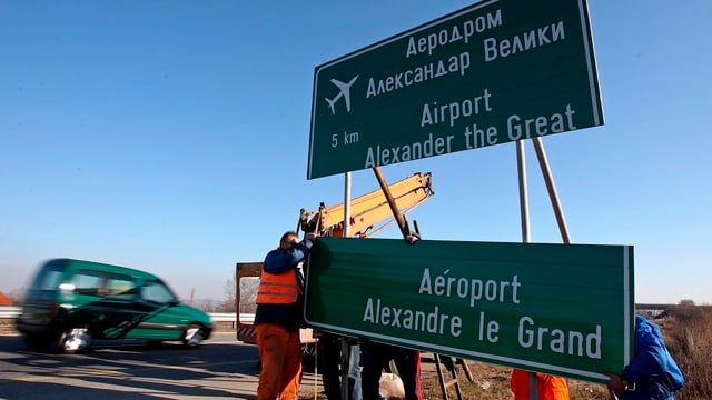 Arbeiter in orangen Westen entfernen das Autobahnschild zum Flughafen in Skopje. Arbeiter in orangen Westen entfernen das Autobahnschild zum Flughafen in Skopje.