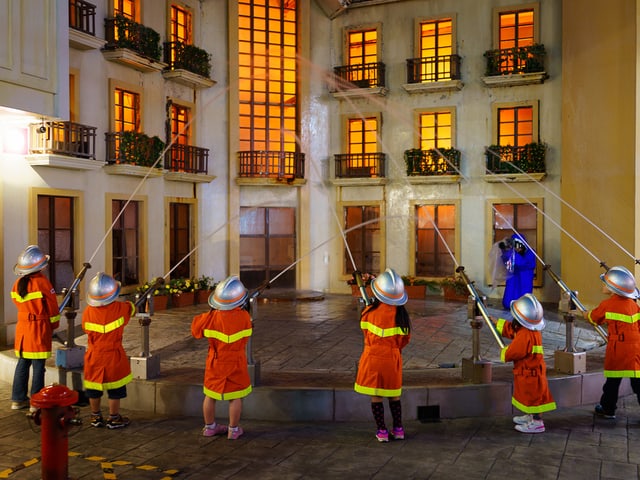 Kinder zielen mit Wasserschläuchen auf ein vermeindlich brennendes Haus. Kinder zielen mit Wasserschläuchen auf ein vermeindlich brennendes Haus.
