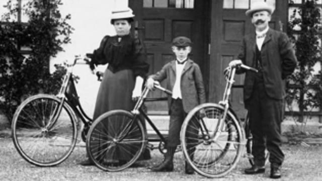 Schwarzweiss-Foto eines Ehepaars mit Sohn. Alle stehen vor einem Velo. Schwarzweiss-Foto eines Ehepaars mit Sohn. Alle stehen vor einem Velo.