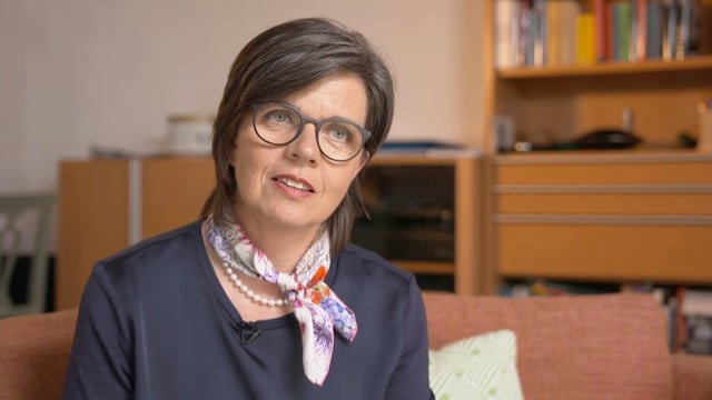 Eine Frau mit Brille und Foulard sitzt auf einem Sofa. Eine Frau mit Brille und Foulard sitzt auf einem Sofa.