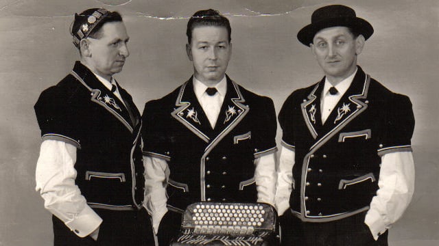 Schwarz-weiss Fotografie mit drei Jodlern in Sennentracht vor einem Akkordeon. Schwarz-weiss Fotografie mit drei Jodlern in Sennentracht vor einem Akkordeon.