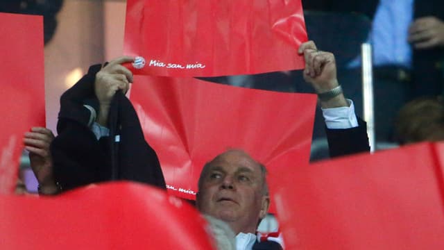 Uli Hoeness hält ein rotes Papier in die Luft. Uli Hoeness hält ein rotes Papier in die Luft.
