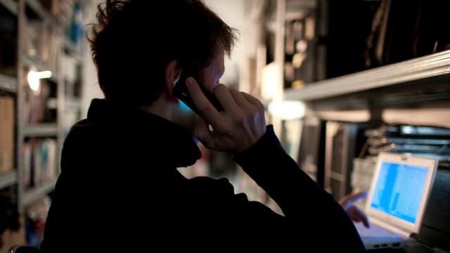 Ein Mann mit Telefon am Ohr sitzt vor einem Computer Ein Mann mit Telefon am Ohr sitzt vor einem Computer