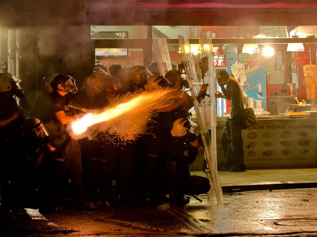 Ein Polizist feuert Tränengas in Richtung Demonstranten Ein Polizist feuert Tränengas in Richtung Demonstranten