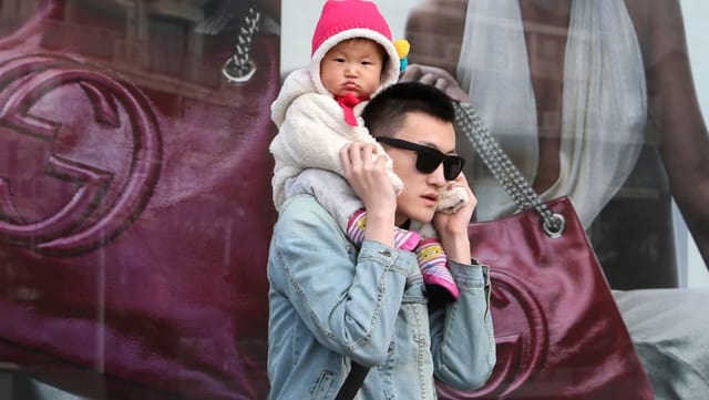 Ein Chinese mit einem Baby auf den Schultern vor einem Gucci-Plakat. Ein Chinese mit einem Baby auf den Schultern vor einem Gucci-Plakat.