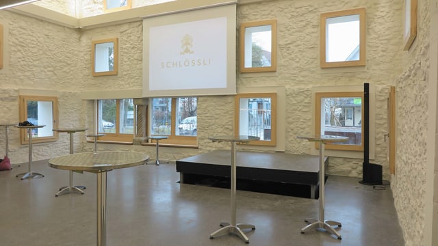 Innenansicht: Kleine Bühne, Leinwand, Stehtische im Raum Innenansicht: Kleine Bühne, Leinwand, Stehtische im Raum