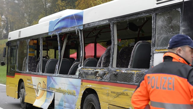 Eingedrückte Fenster des Postautobusses, rechts vorne ein Polizist. Eingedrückte Fenster des Postautobusses, rechts vorne ein Polizist.