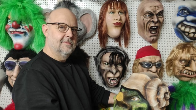 Mann vor Wand mit Masken Mann vor Wand mit Masken