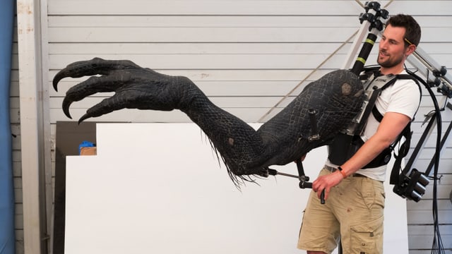 Ein Mann trägt eine riesige Dinosaurier-Kralle vor sie her. Mit hebeln kann er die einzelnen Teile bewegen.