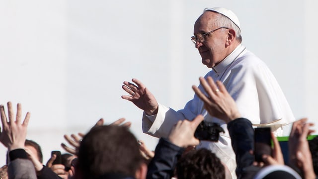 Nahaufnahme des Papstes Franziskus, der mit dem Papamobil durch die Massen fährt und die Menschen grüsst.