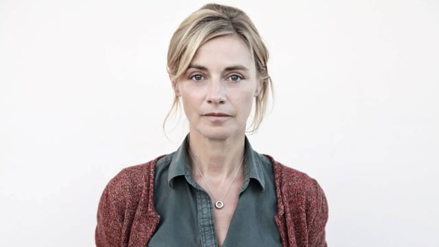 Eine Frau mit blonden Haaren und roter Jacke steht vor einer weissen Wand. Eine Frau mit blonden Haaren und roter Jacke steht vor einer weissen Wand.