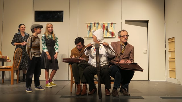 Szene in einem Landtheater: Links stehen zwei Kinder auf der Bühne, im Vordergrund sitzen drei Männer. Einer ist als Wilhelm Tell verkleidet und hält eine Armbrust. Szene in einem Landtheater: Links stehen zwei Kinder auf der Bühne, im Vordergrund sitzen drei Männer. Einer ist als Wilhelm Tell verkleidet und hält eine Armbrust.